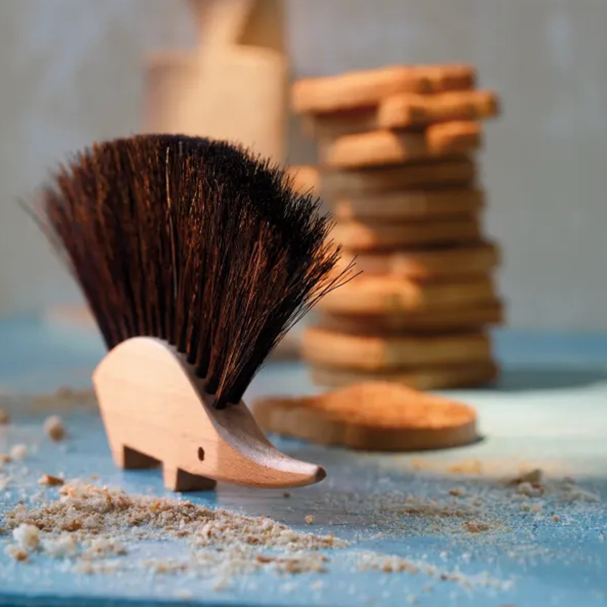 Wooden table brush with bristles on a blue surface with wooden in the background.