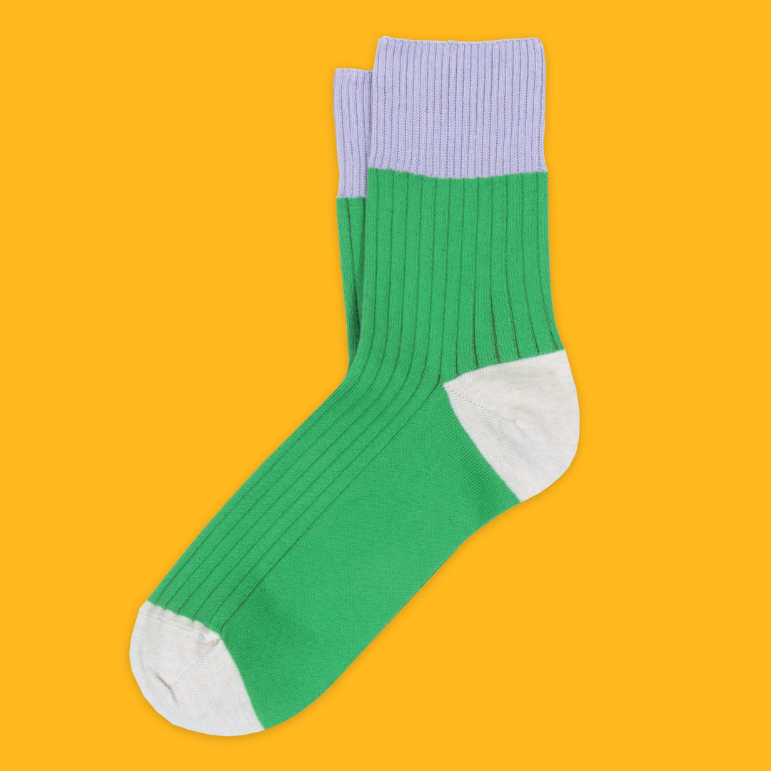 Green socks with white toes and purple cuffs on a yellow background