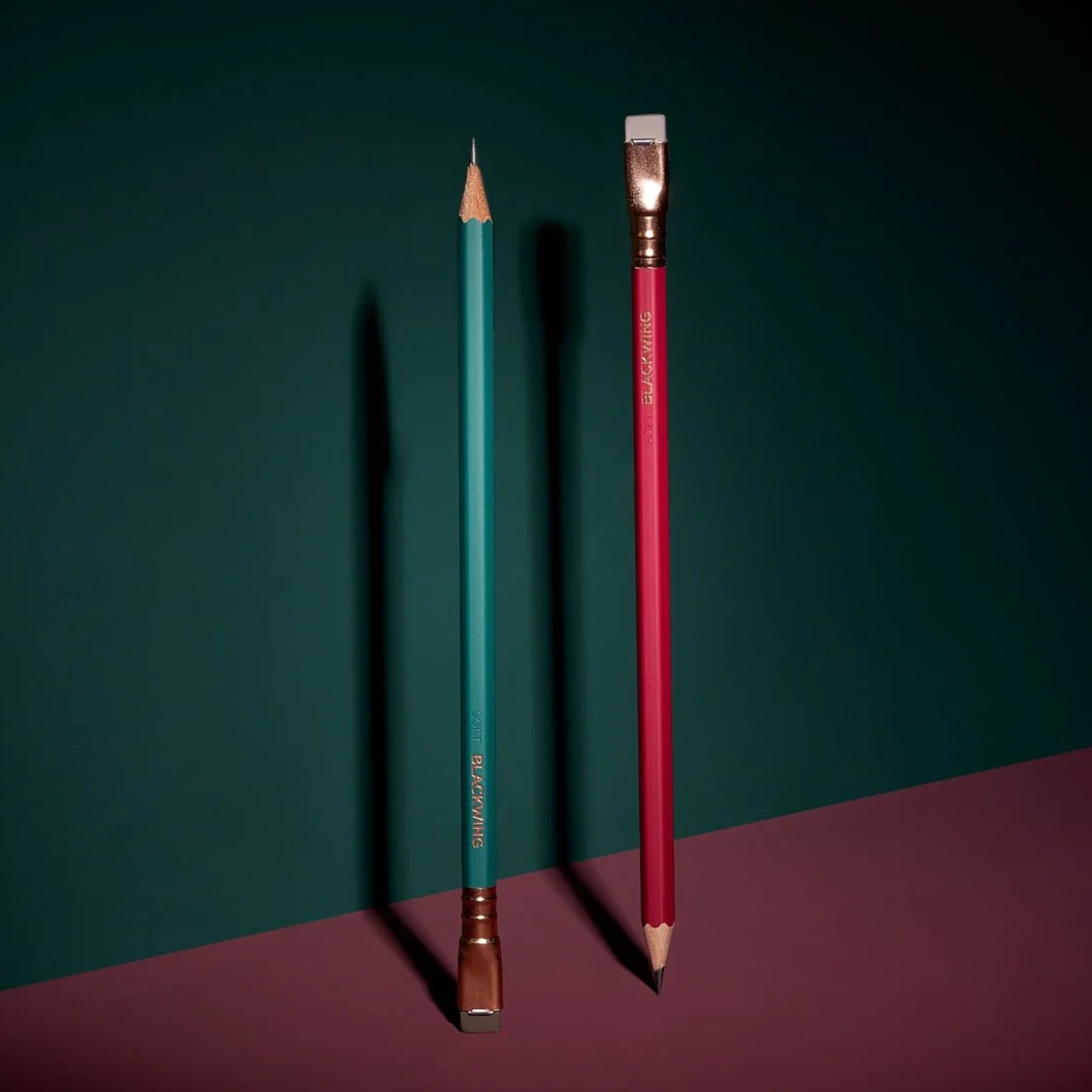 Two pencils, one green and one red, on a dark green and purple surface.