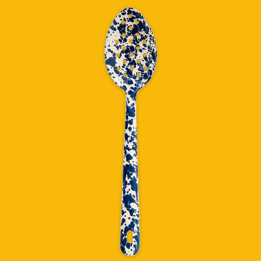 Enamel Splatter Navy and Cream slotted spoon on a yellow background
