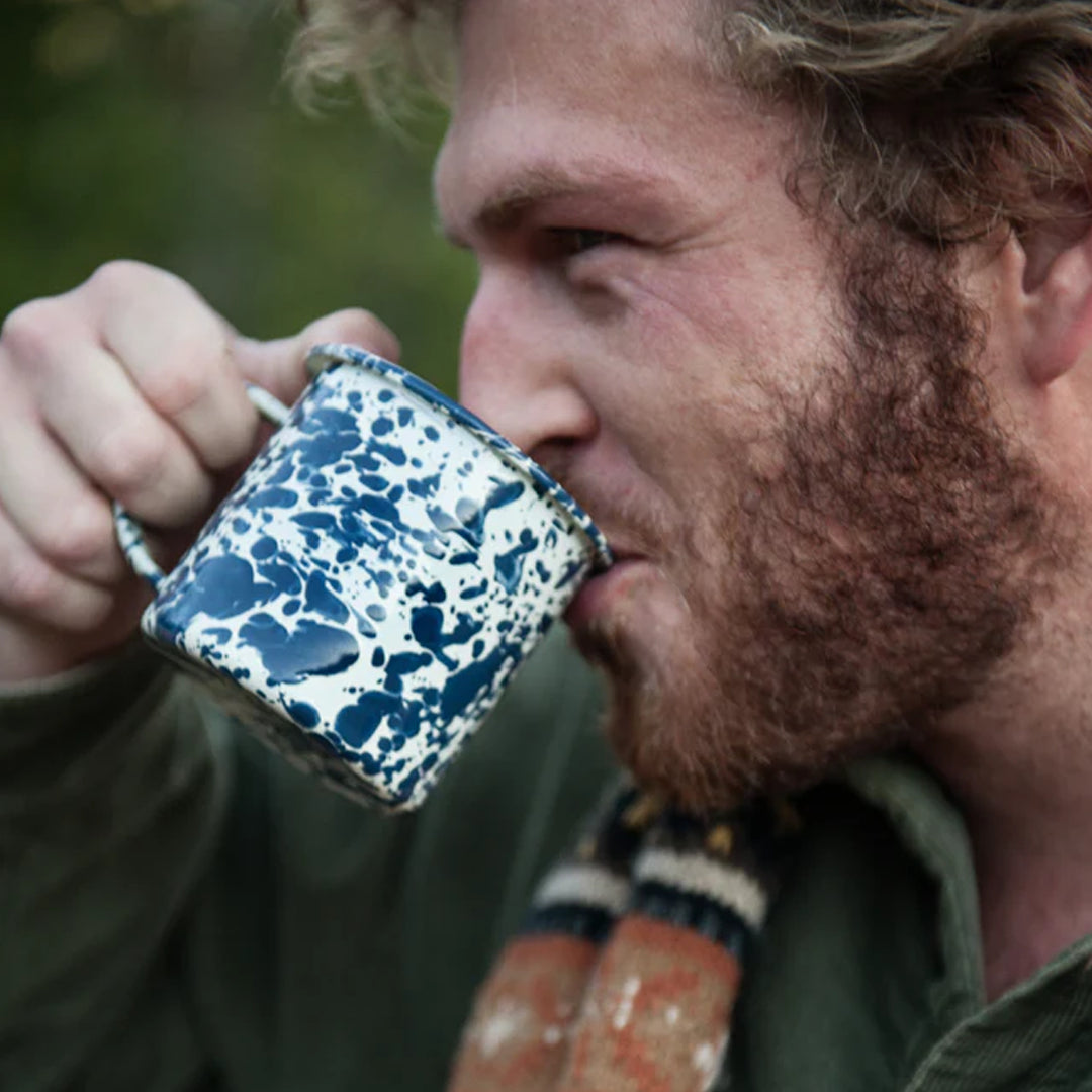 Man drinking from a navy and cream speckled mug outdoors