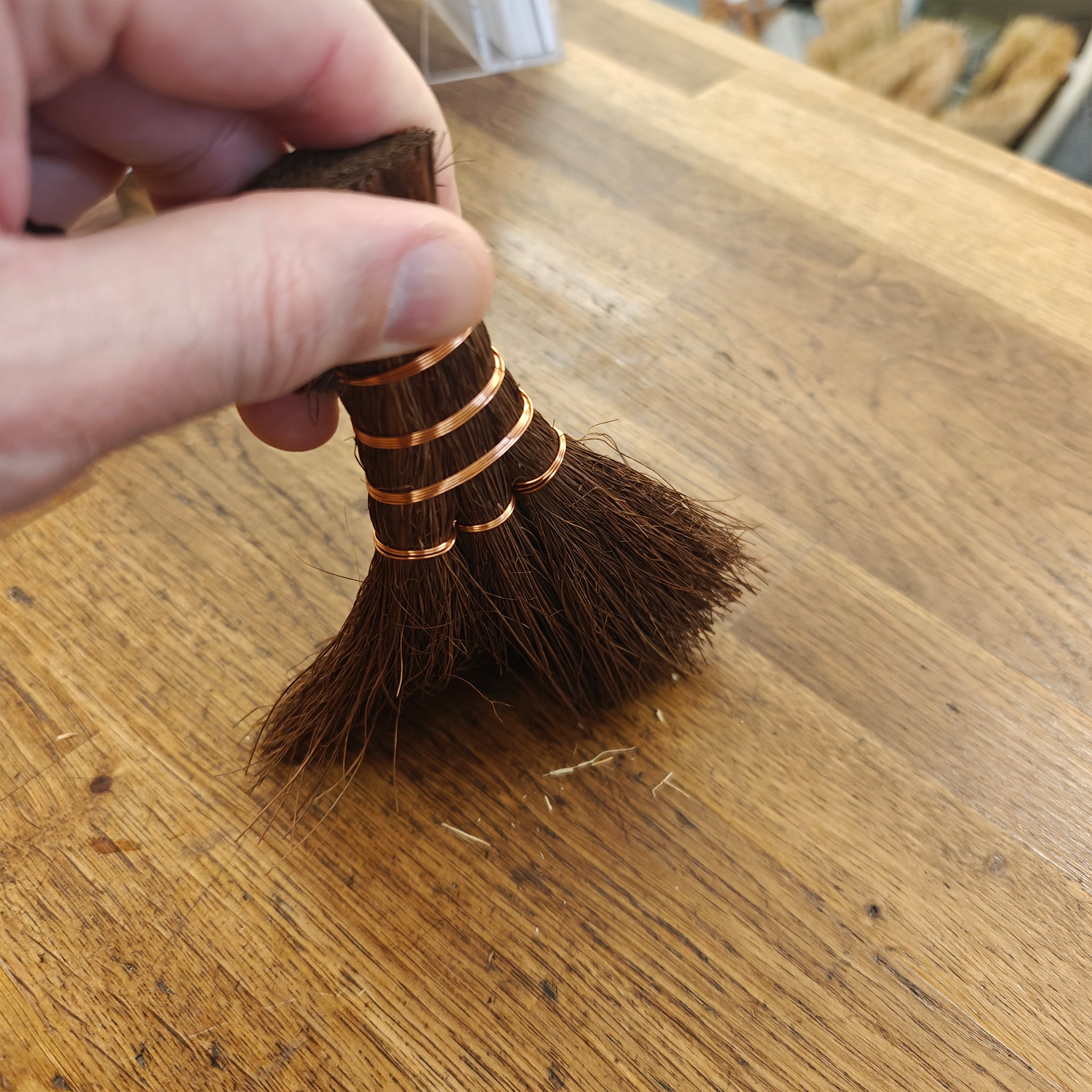Small brush with brown bristles held by a hand on a wooden surface