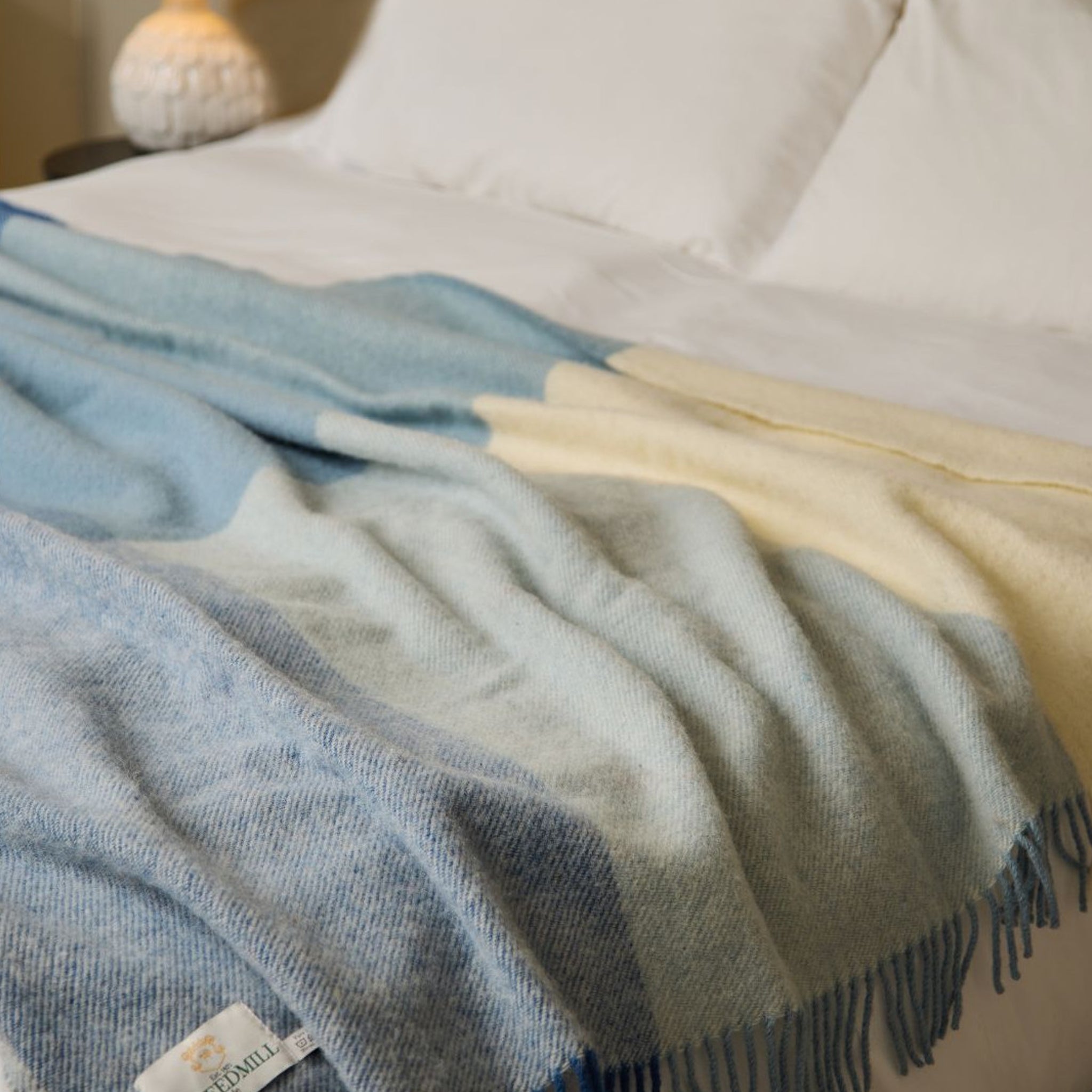 Check blanket with blue, light blue, and beige colours draped over a bed.