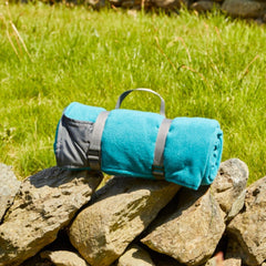 Fleece Picnic Rug Roll in Teal on a stone wall