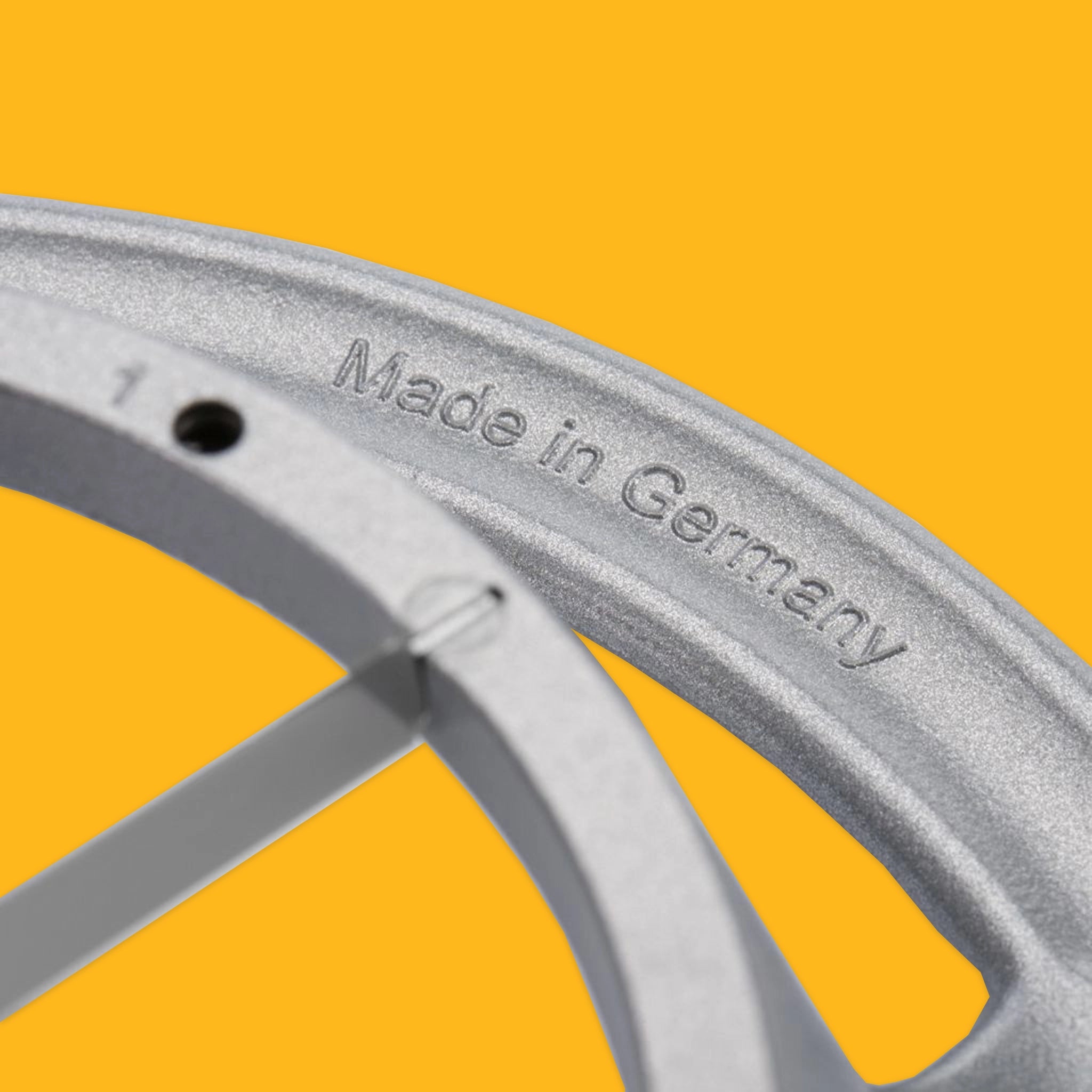 Close-up of a silver metal wheel rim with the text 'Made in Germany' embossed on the inner edge, set against a solid bright yellow background.