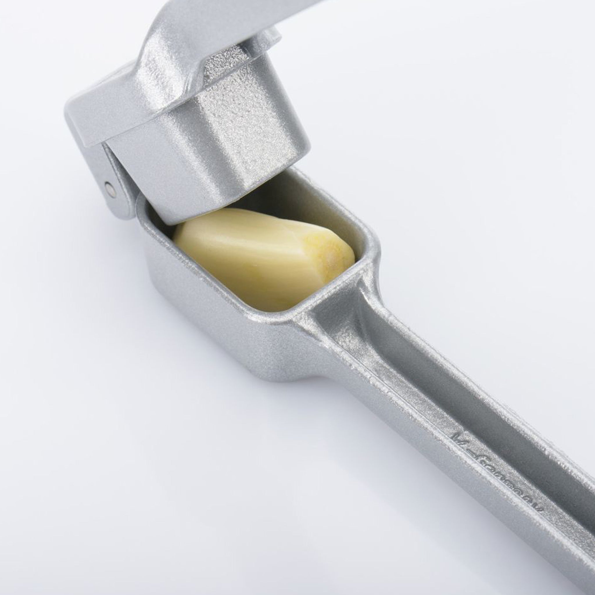 Silver garlic press with a clove of garlic inside on a white background