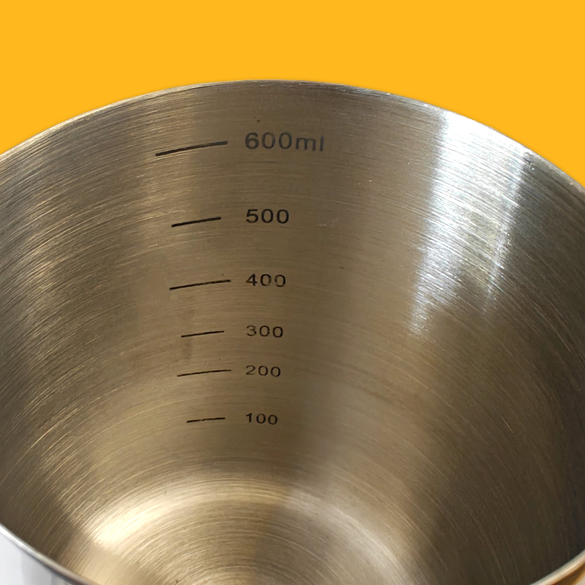 Metal measuring jug with volume markings on a yellow background